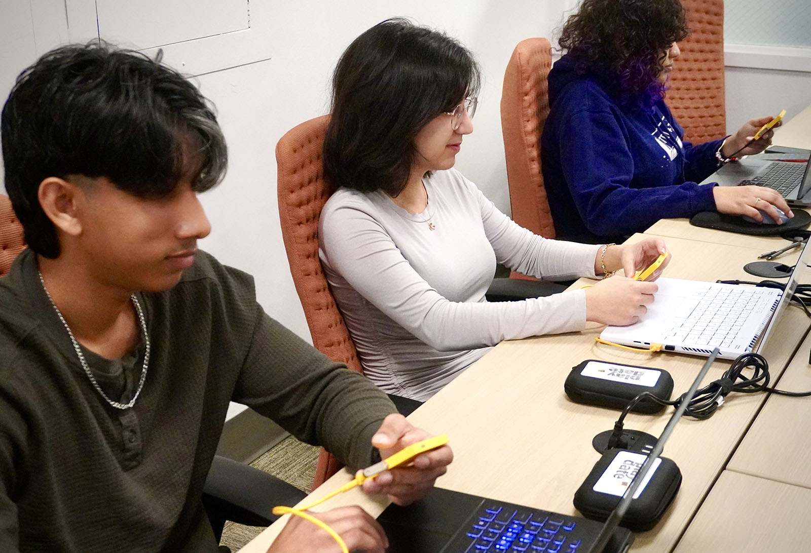Three Duke GDDI students developing games using the Playdate handheld console and their laptops.